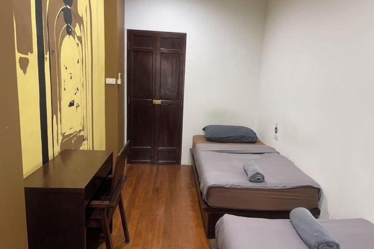 Una habitación pequeña y funcional con un escritorio de madera, dos camas individuales y un armario.