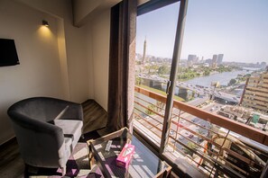 A room with a view of a cityscape, a chair, a small table with a box, and a window with a curtain. - Nile Boutique hotel (Giza)