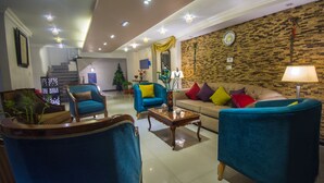 A modern living room with blue armchairs, a beige sofa with colorful cushions, a wooden coffee table, and a brick-patterned wall. - Nile Boutique hotel (Giza)