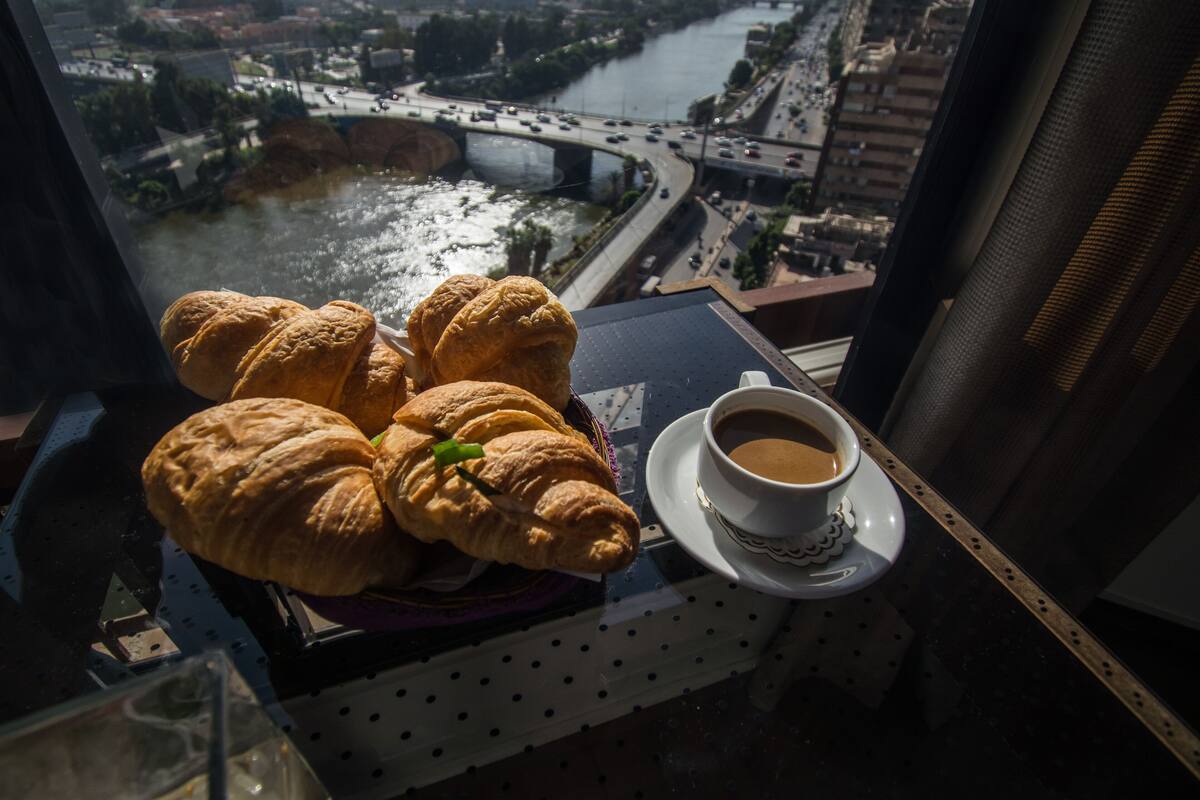 A table with croissants and a cup of coffee, overlooking a cityscape with a river and bridge.