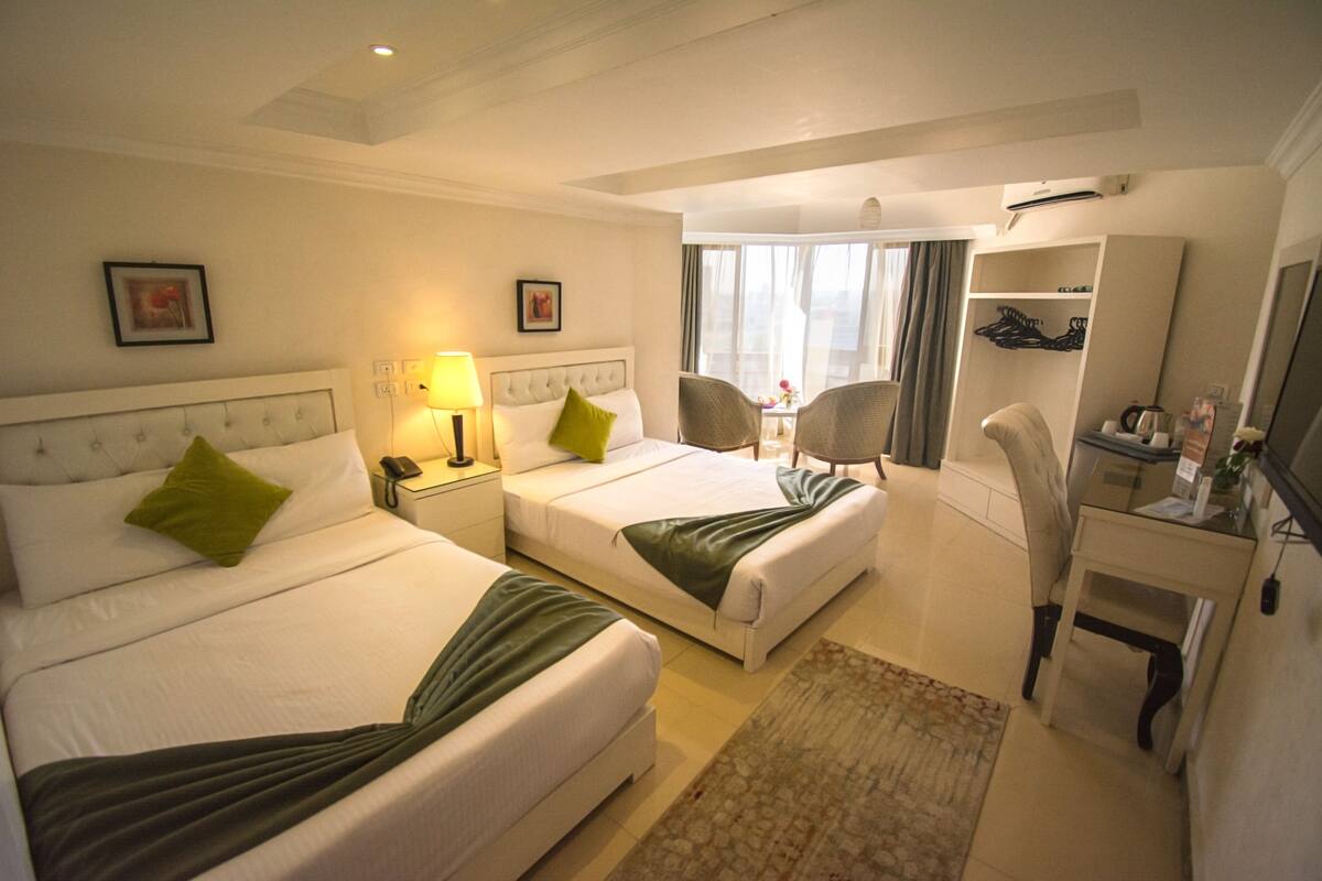A hotel room with two beds, a desk, a chair, a wardrobe, and a bathroom.
