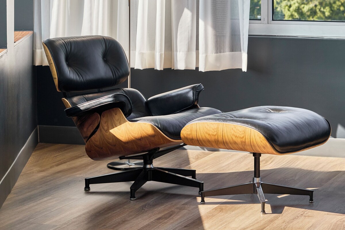Ein modernes Zimmer mit Ledersessel, Stehlampe und Blick durch ein Fenster mit leichtem Vorhang.