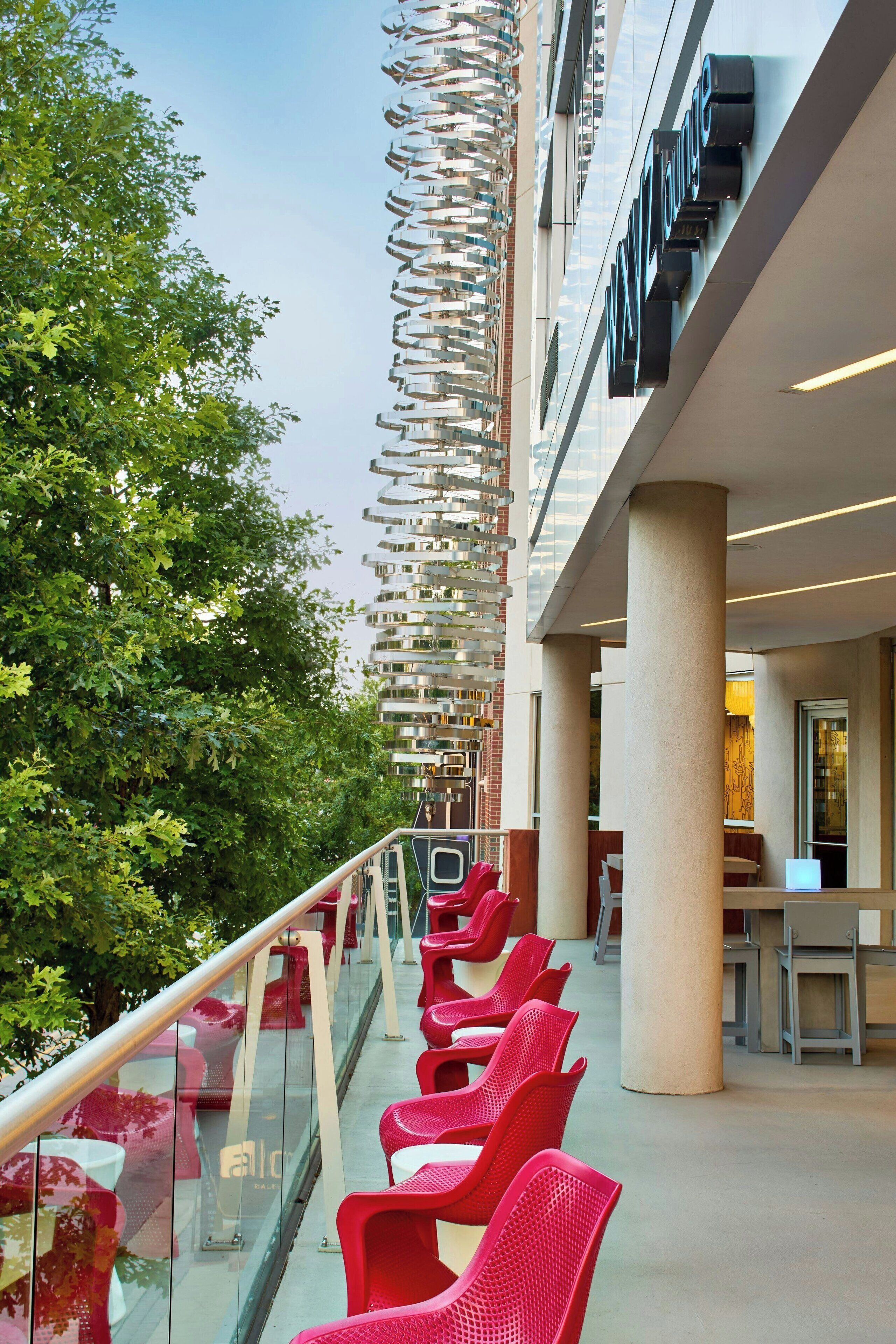 Ein modernes Hotel-Atrium mit Glastrennwand, roten Stühlen und einer vertikalen Gartenanlage.