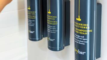 A hand adjusting a black pump dispenser on a wall-mounted shelf with three bottles of hair care products.