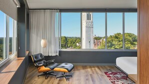 A modern hotel room with a large window, a bed, a desk, and a chair.