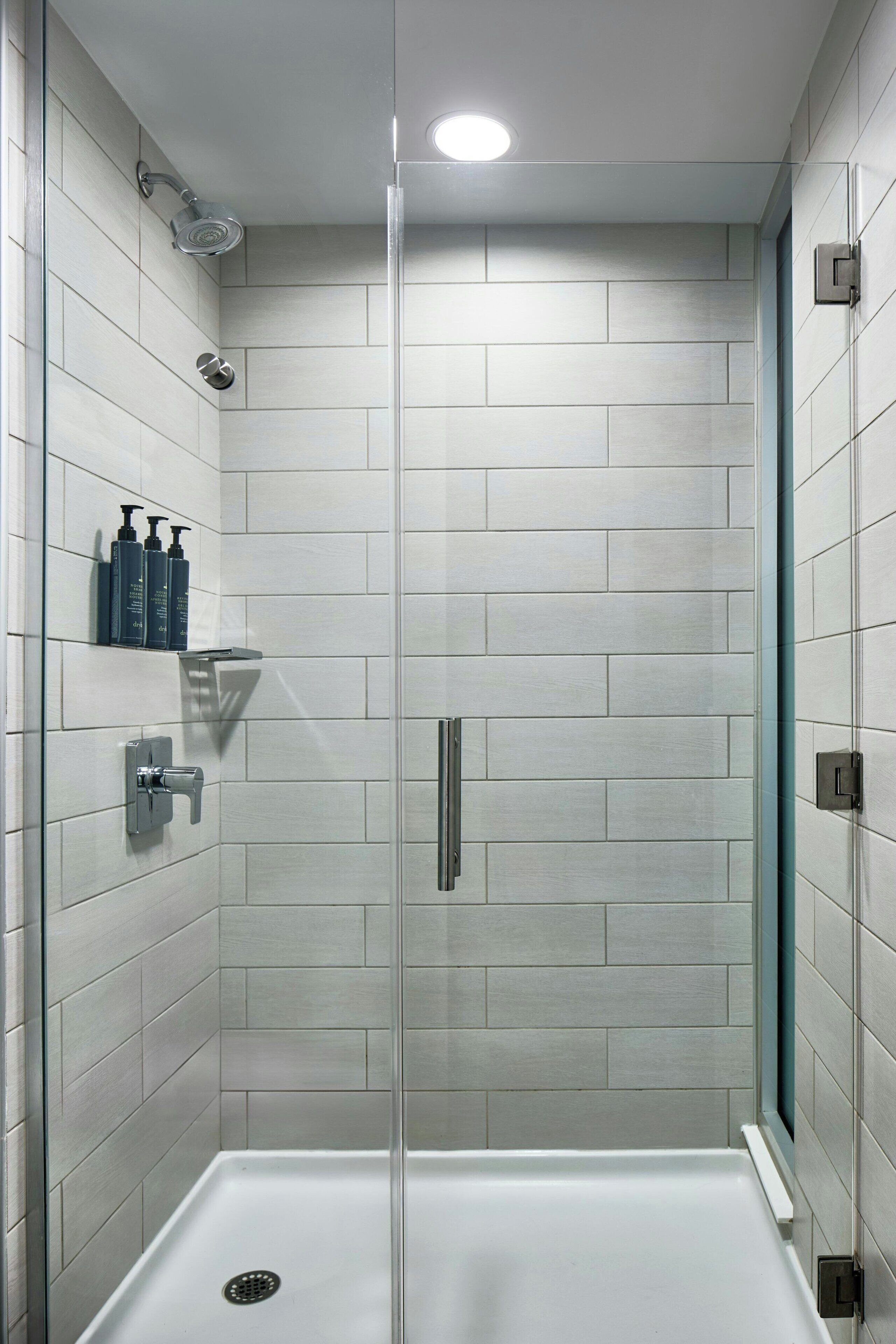 A modern shower with a glass door, a built-in shelf with toiletries, and a control panel for water temperature and flow.