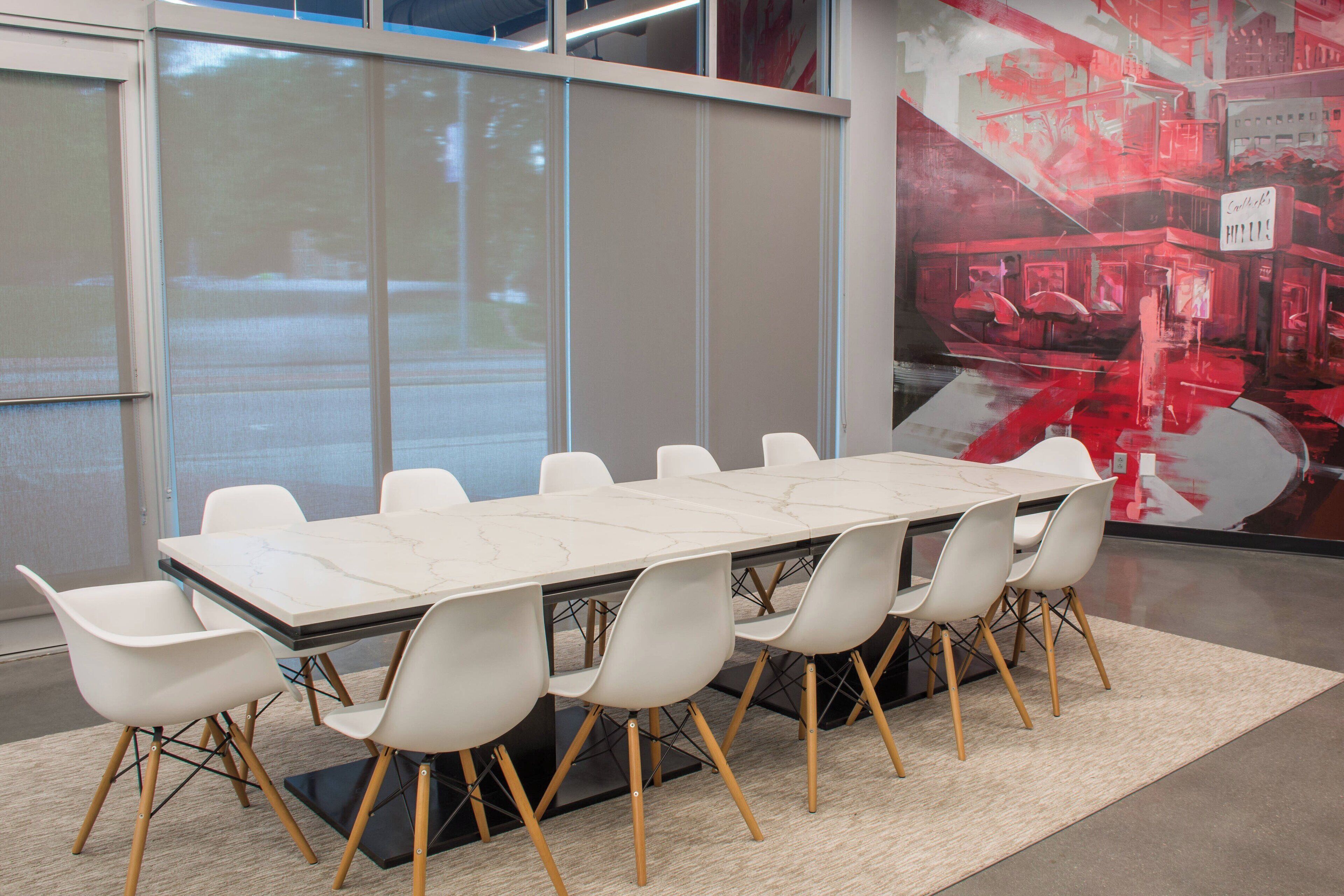 A conference room with a marble table and white chairs, large windows, and a cityscape mural.