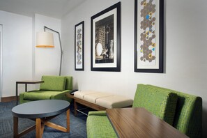 A modern hotel room with a green sofa, a round table, and three framed artworks on the wall. - Holiday Inn Express & Suites Bay City by IHG (Bay City)