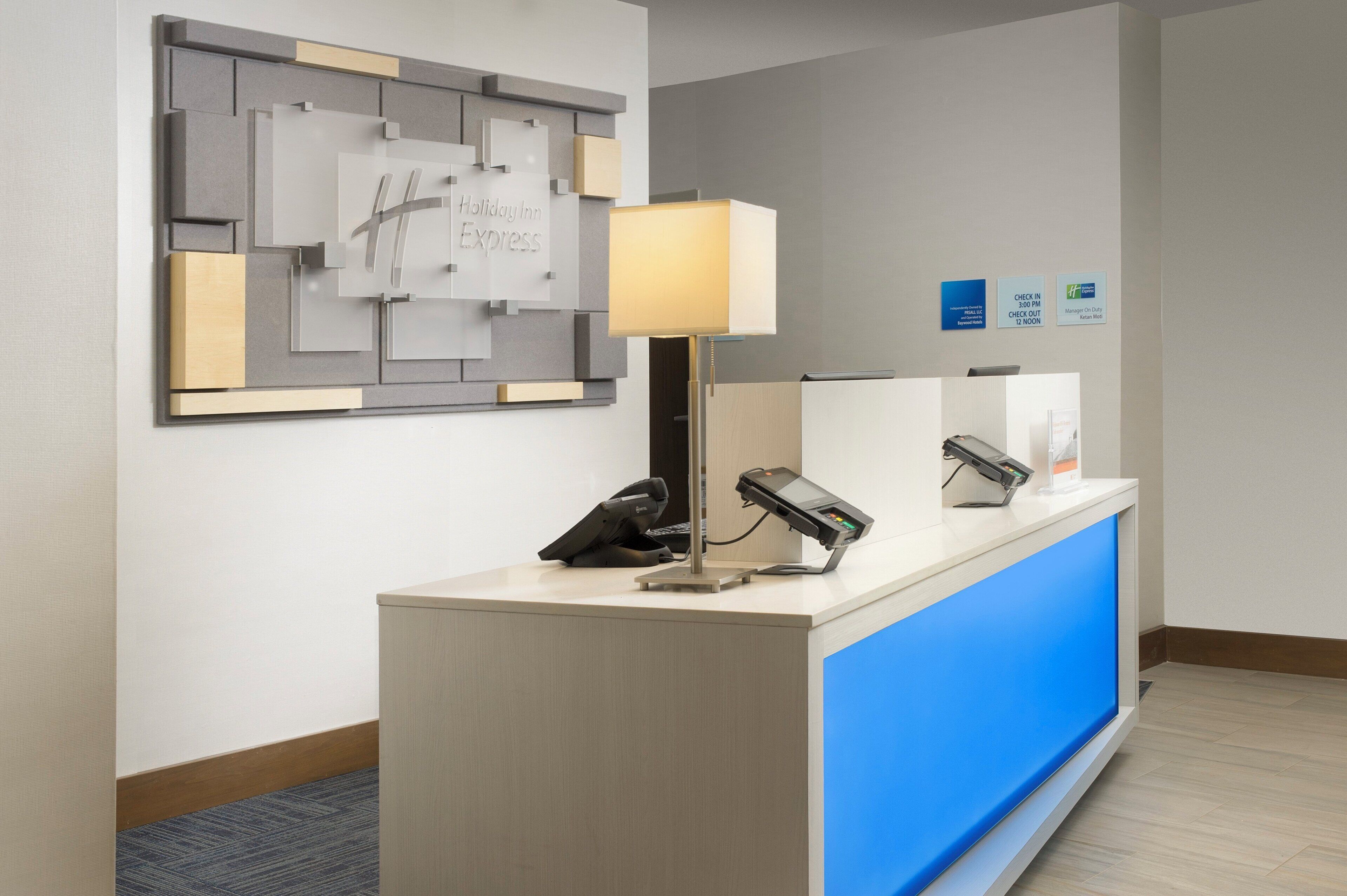 Mostrador de recepción de hotel con detalles azules, un teléfono, una lámpara y un letrero en la pared.