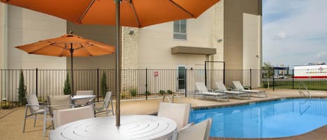 A poolside area with a round table and chairs, two orange umbrellas, and a pool.