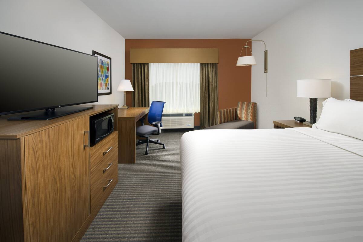 A hotel room with a large flat-screen TV, a desk with a chair, a bed, and two bedside lamps.