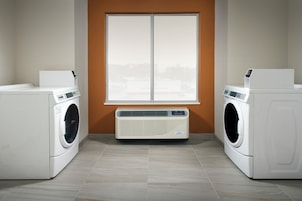 A laundry room with two washing machines, a dryer, and a large window.