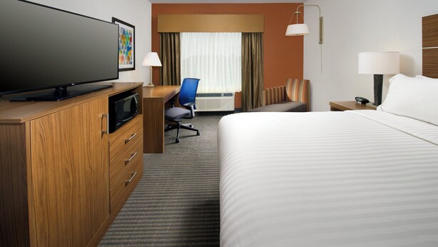 A hotel room with a bed, a desk with a computer, a television, a chair, and a window with curtains. - Holiday Inn Express & Suites Bay City by IHG (Bay City)