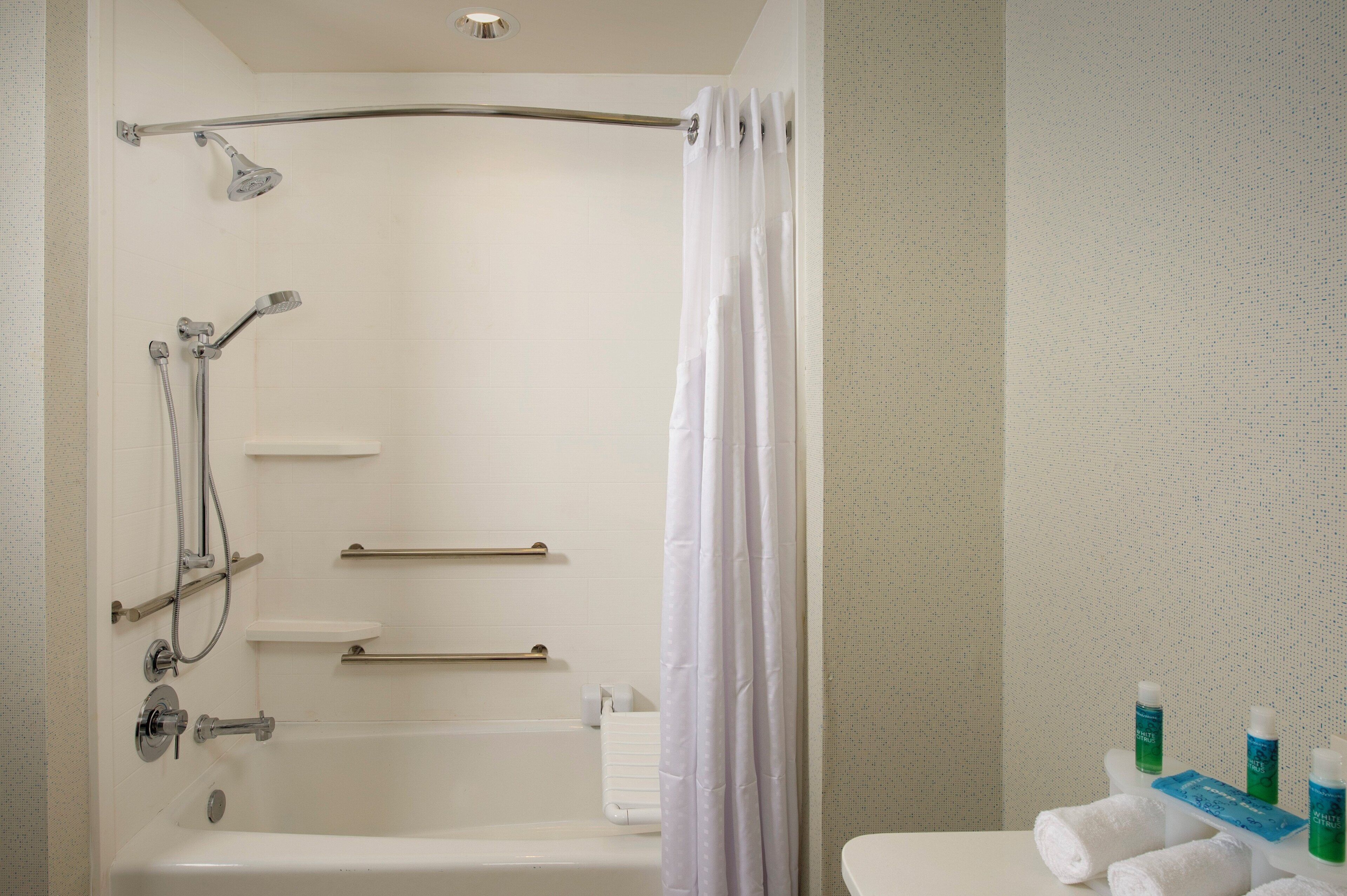 Een badkamer met een bad, douche en toilet. Er zijn handgrepen, een handdoekhouder en een douchegordijn.