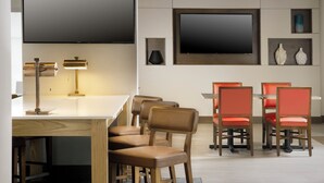 A modern dining area with a white table and red chairs, a flat-screen TV mounted on the wall, and a lamp on the table. - Holiday Inn Express & Suites Bay City by IHG (Bay City)