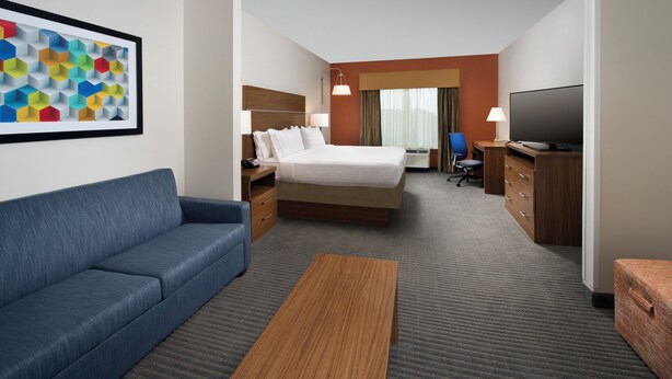 Ein Hotelzimmer mit einem Bett, einem blauen Sofa, einem Holztisch, einem Fernseher und einem Schreibtisch mit Schubladen.
