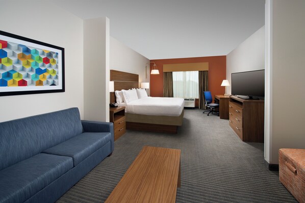 A hotel room with a bed, a blue sofa, a wooden coffee table, a TV, and a desk with drawers. - Holiday Inn Express & Suites Bay City by IHG (Bay City)