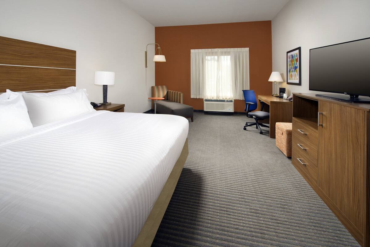 A hotel room with a large bed, a desk with a computer, a TV, and a window with curtains.