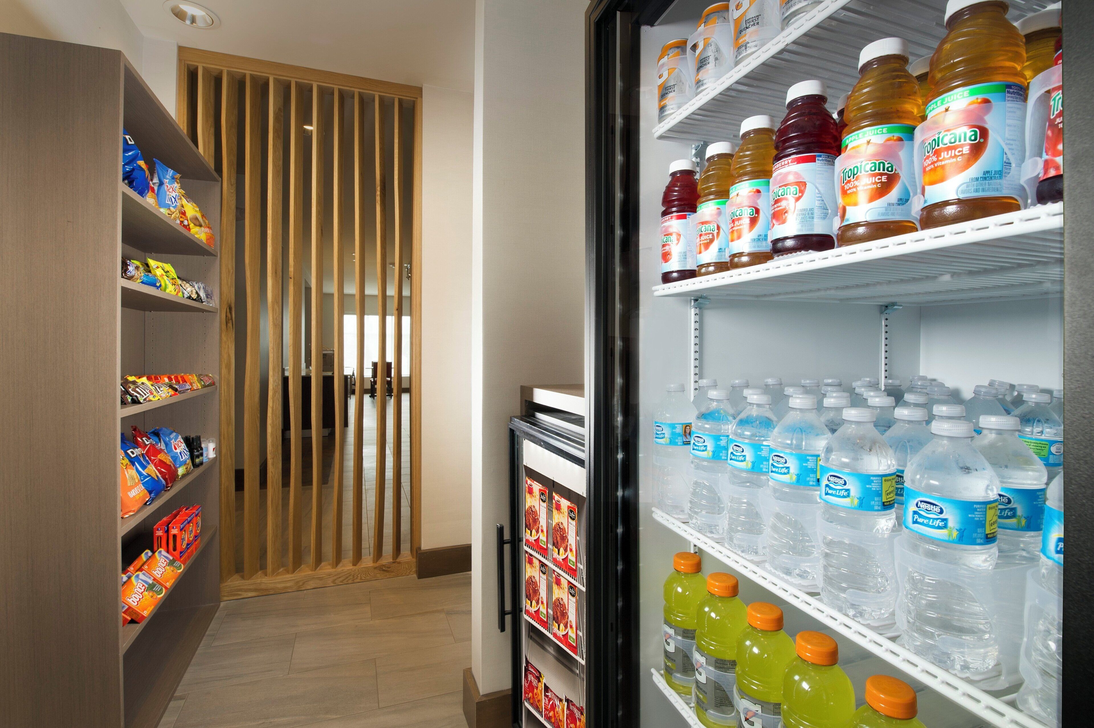 A hotel room with a minibar stocked with snacks, beverages, and a refrigerator containing various drinks.