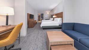 Et hotelværelse med seng, skrivebord, stol, sofa og fjernsyn.