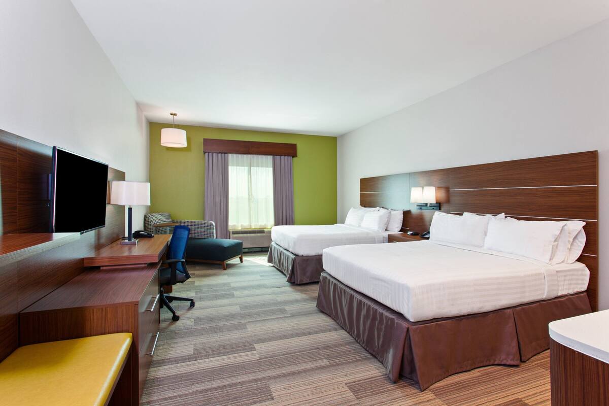 A hotel room with two beds, a desk with a TV, a chair, and a small table.