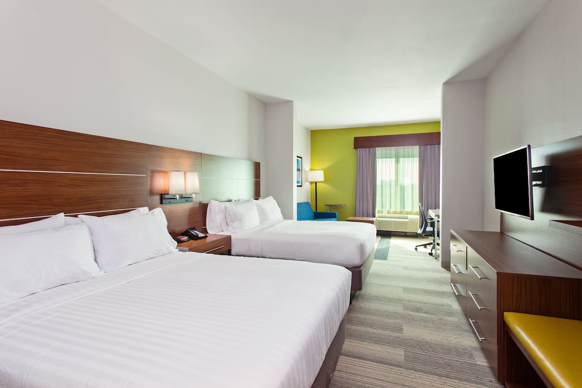A hotel room with two beds, a desk with a lamp, a TV, and a chair.
