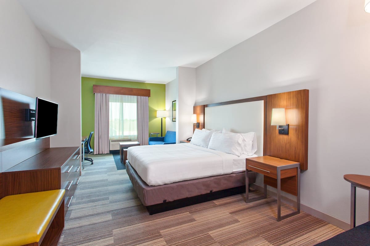 A hotel room with a large bed, a desk, a chair, a TV, and a window with curtains.