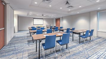 A conference room with multiple tables and chairs, a projector screen, and a carpeted floor.