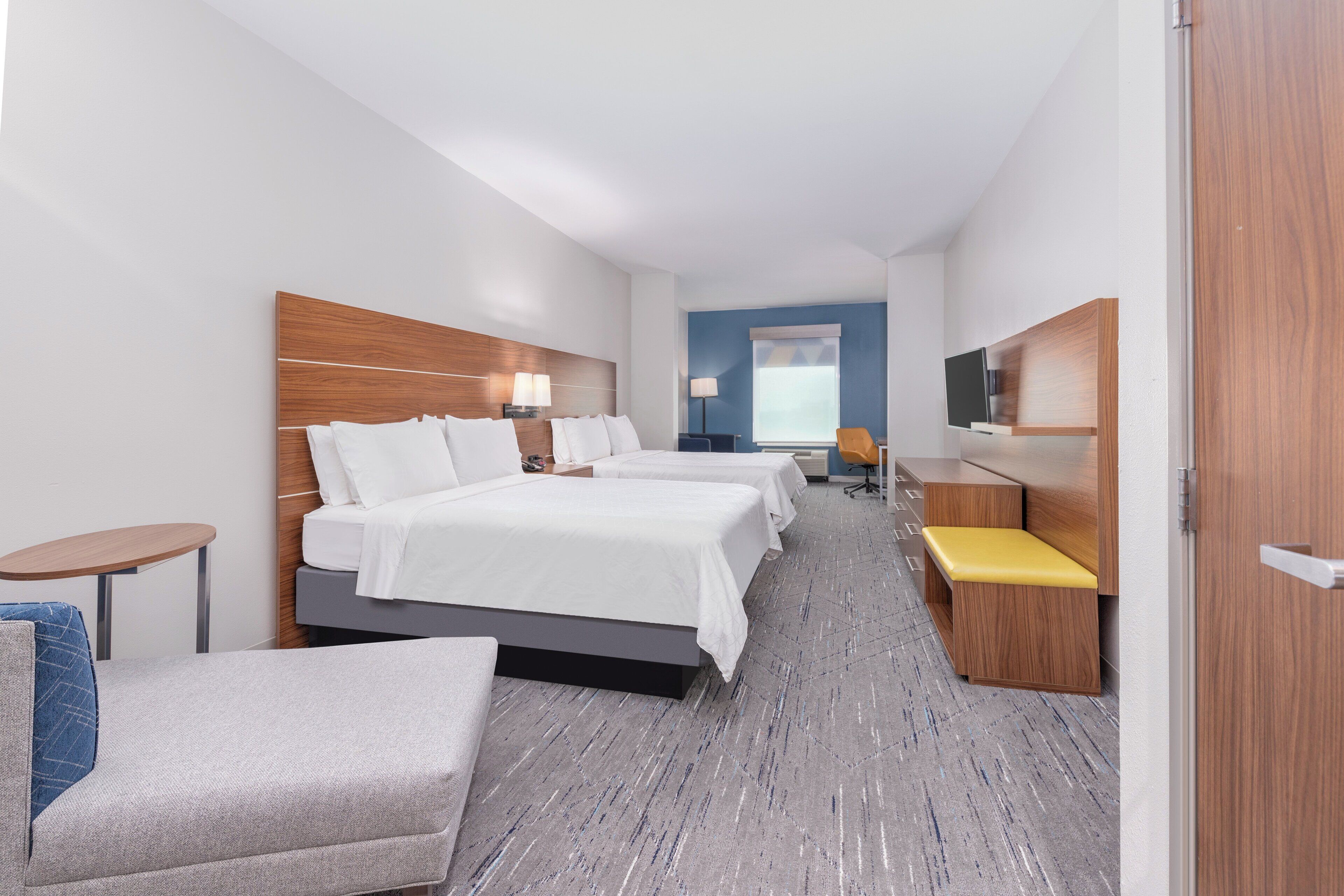 A hotel room with three beds, a sofa, a small table, and a TV.