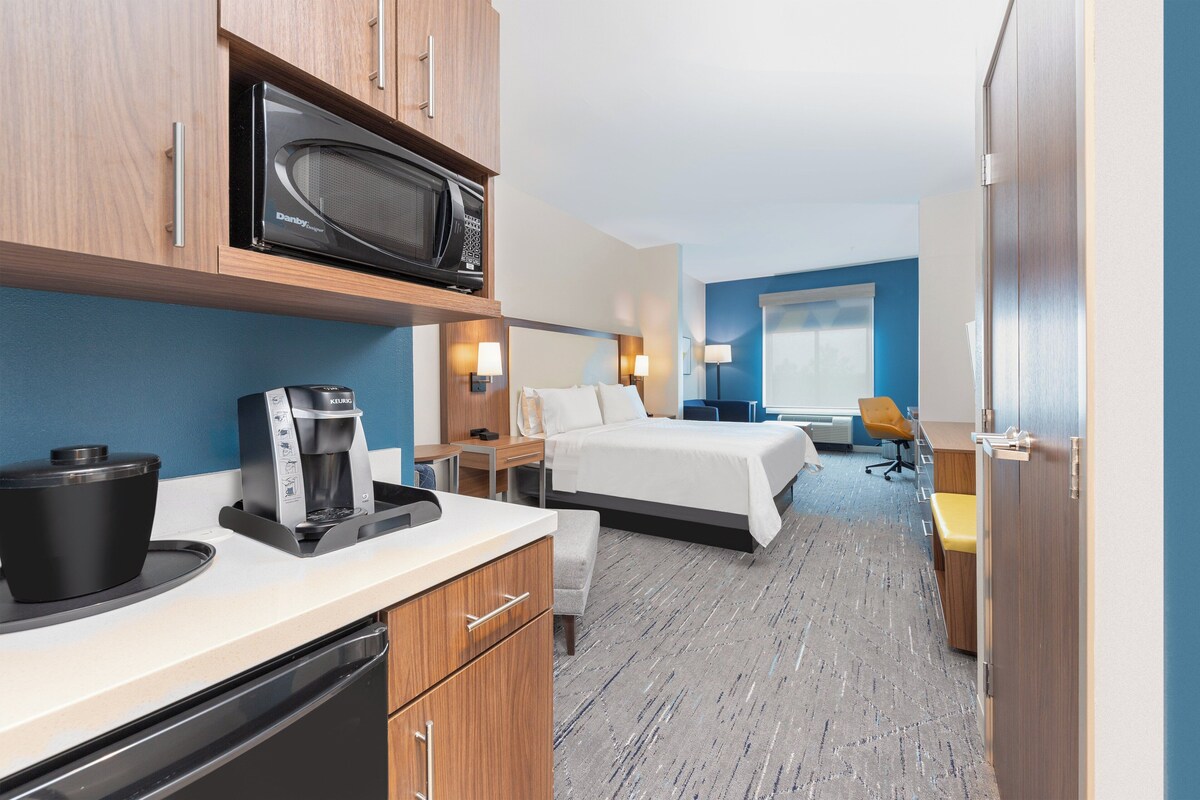 A hotel room with a kitchenette, a bed, a desk, and a chair.