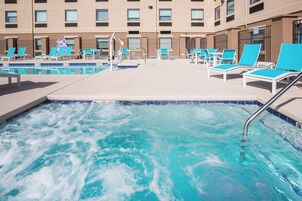 A hotel pool area with multiple lounge chairs and a hot tub.