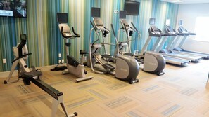 A gym with various cardio machines, a television mounted on the wall, and a patterned carpet. - Holiday Inn Express & Suites Pahrump by IHG (Pahrump)