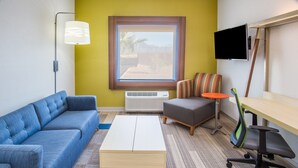 A modern room with a blue sofa, a white coffee table, a grey armchair, a small orange table, and a TV mounted on the wall. - Holiday Inn Express & Suites Pahrump by IHG (Pahrump)