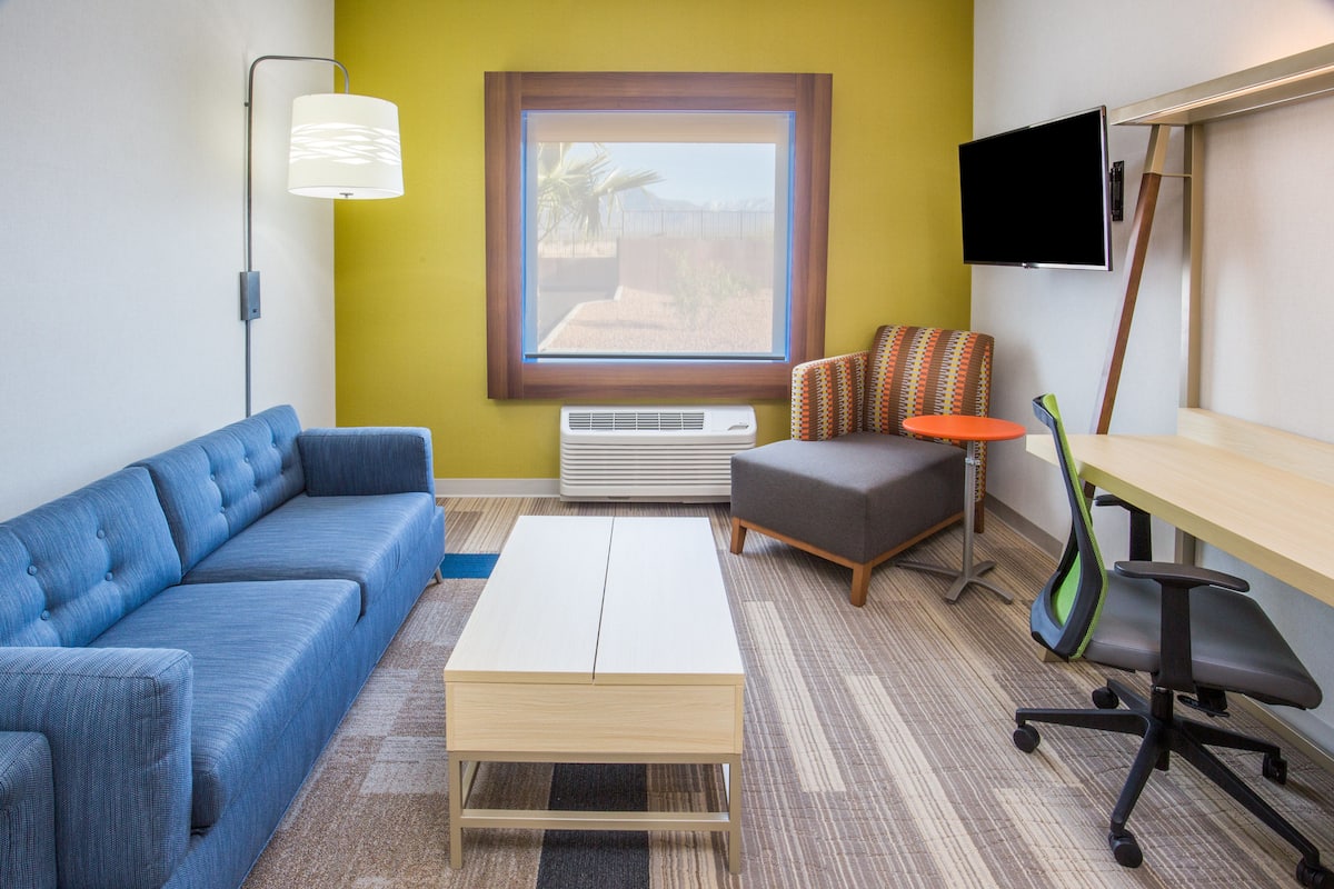 A modern room with a blue sofa, a white coffee table, a grey armchair, a small orange table, and a TV mounted on the wall.