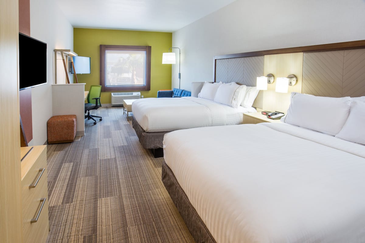A hotel room with two beds, a desk, a chair, a TV, and a window.