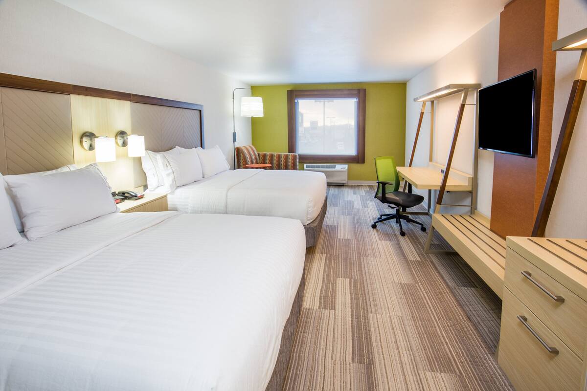 A hotel room with two beds, a desk, a chair, a TV, and a window.