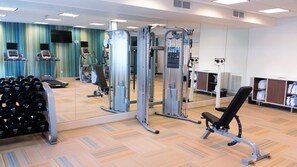 Une salle de sport équipée de machines de cardio, de matériel de musculation et d’un banc.