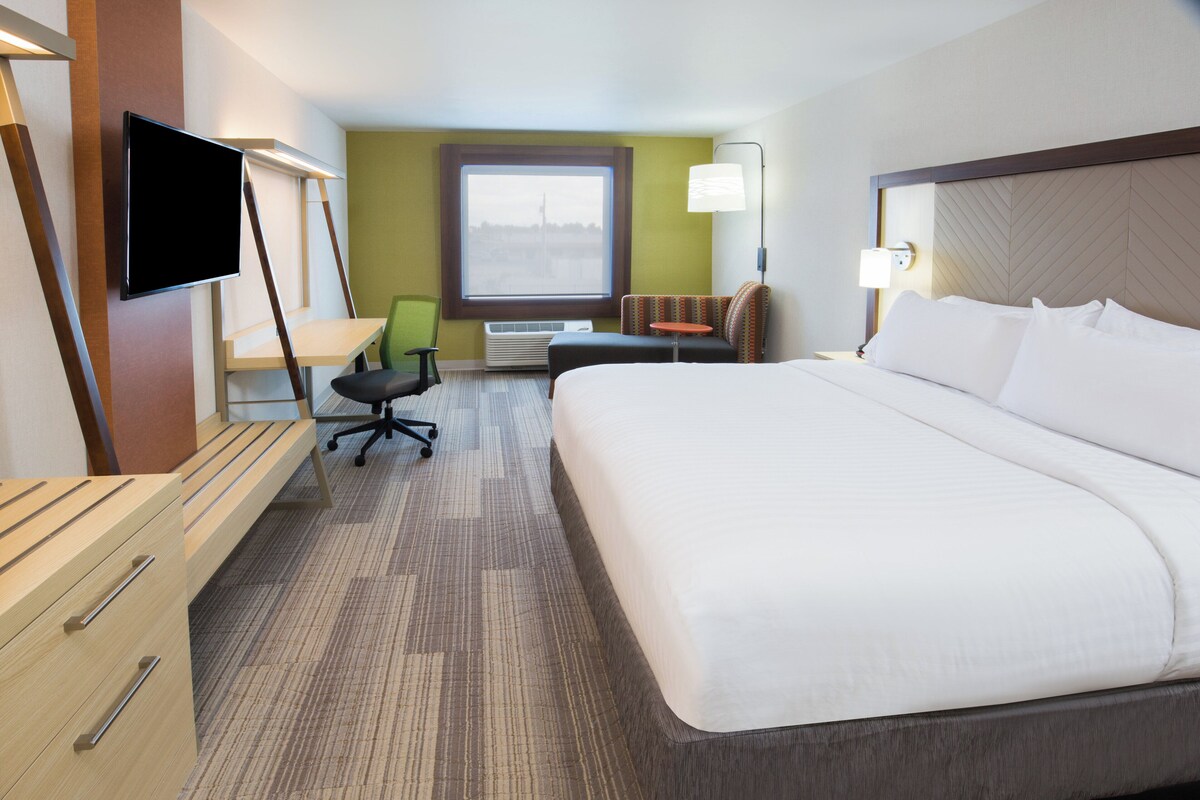 A hotel room with a bed, desk, chair, TV, and a window with a view.
