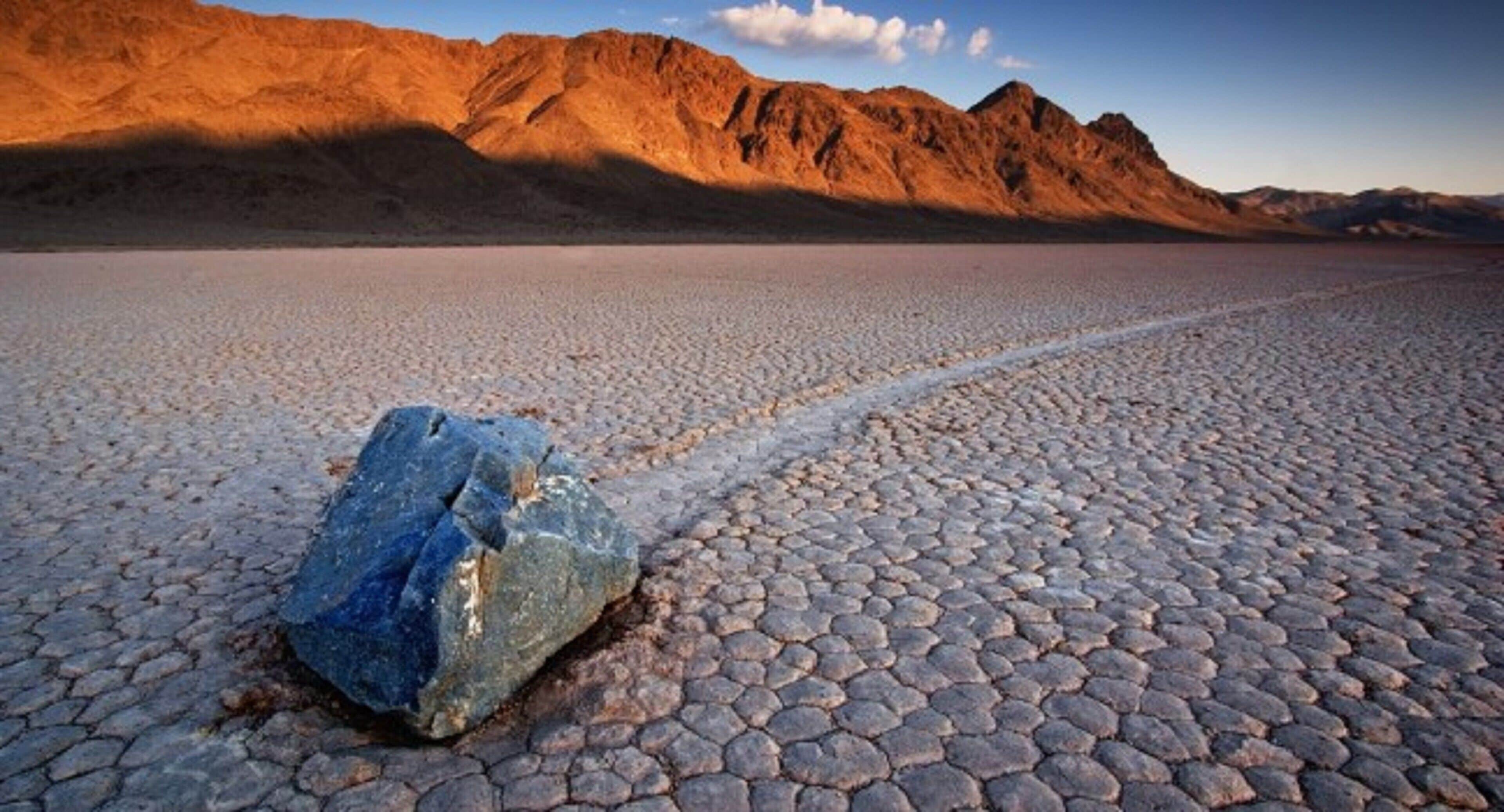 Una extensa planicie salada con una roca destacada en primer plano y montañas al fondo.