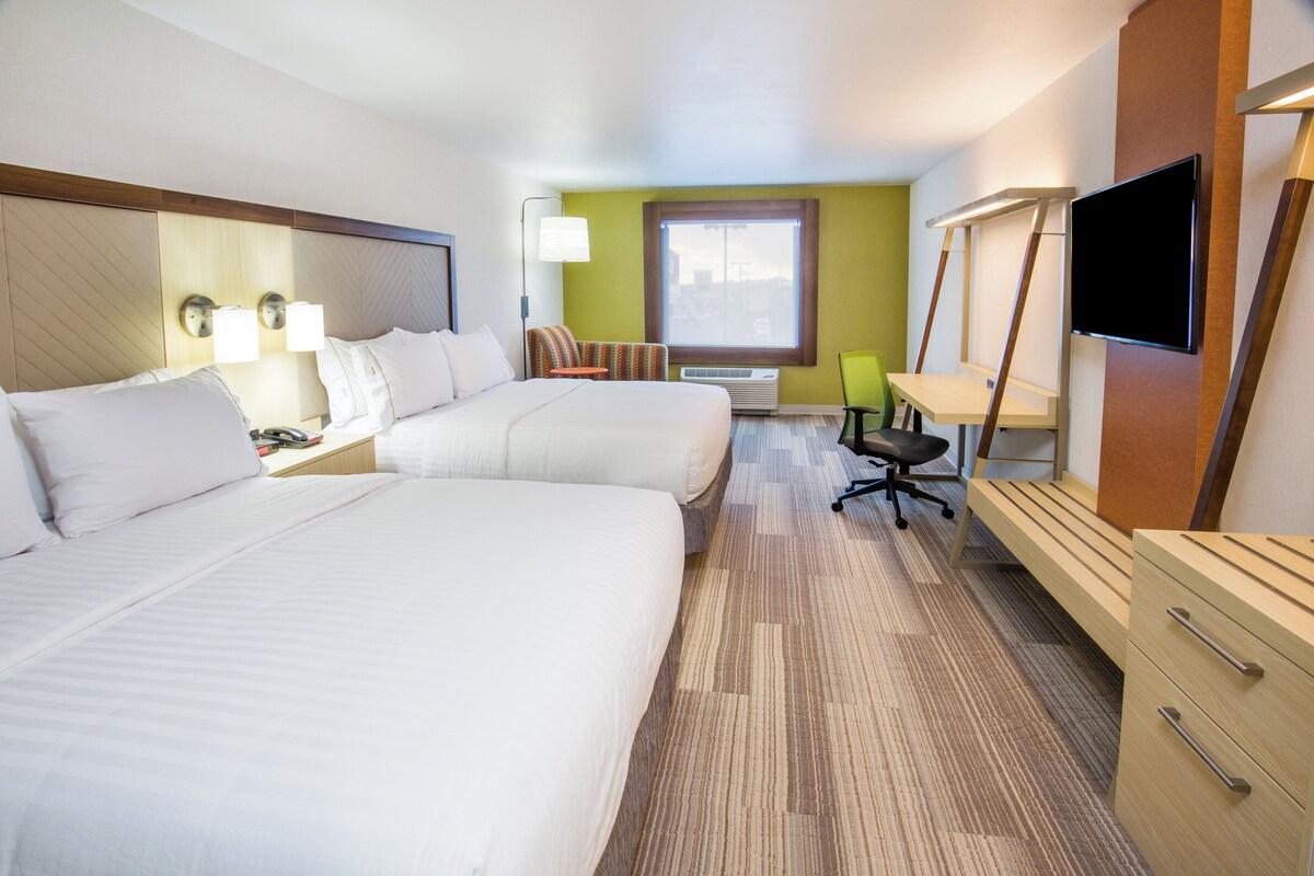 A hotel room with two beds, a desk, a chair, a TV, and a window.