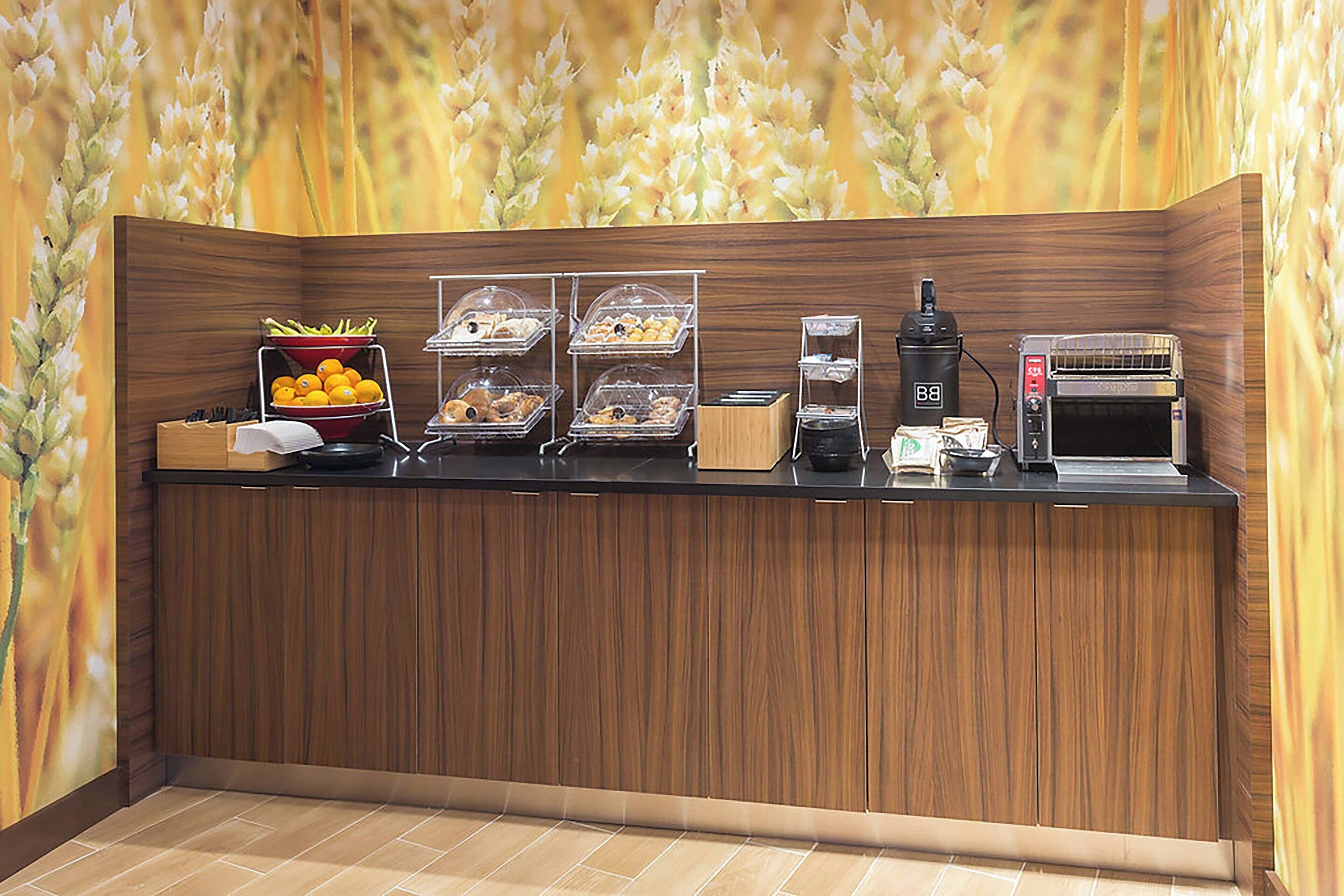 A breakfast bar with trays of pastries, a coffee machine, and a toaster.