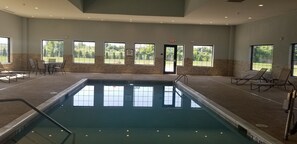 Une grande piscine intérieure aux parois en verre transparent, dotée de nombreuses fenêtres et d’une porte signalée par un panneau indiquant la sortie.
