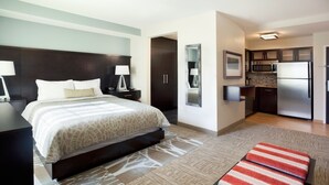 Une chambre d’hôtel comprenant un lit, des tables de chevet, un miroir, une kitchenette et une salle de bain.