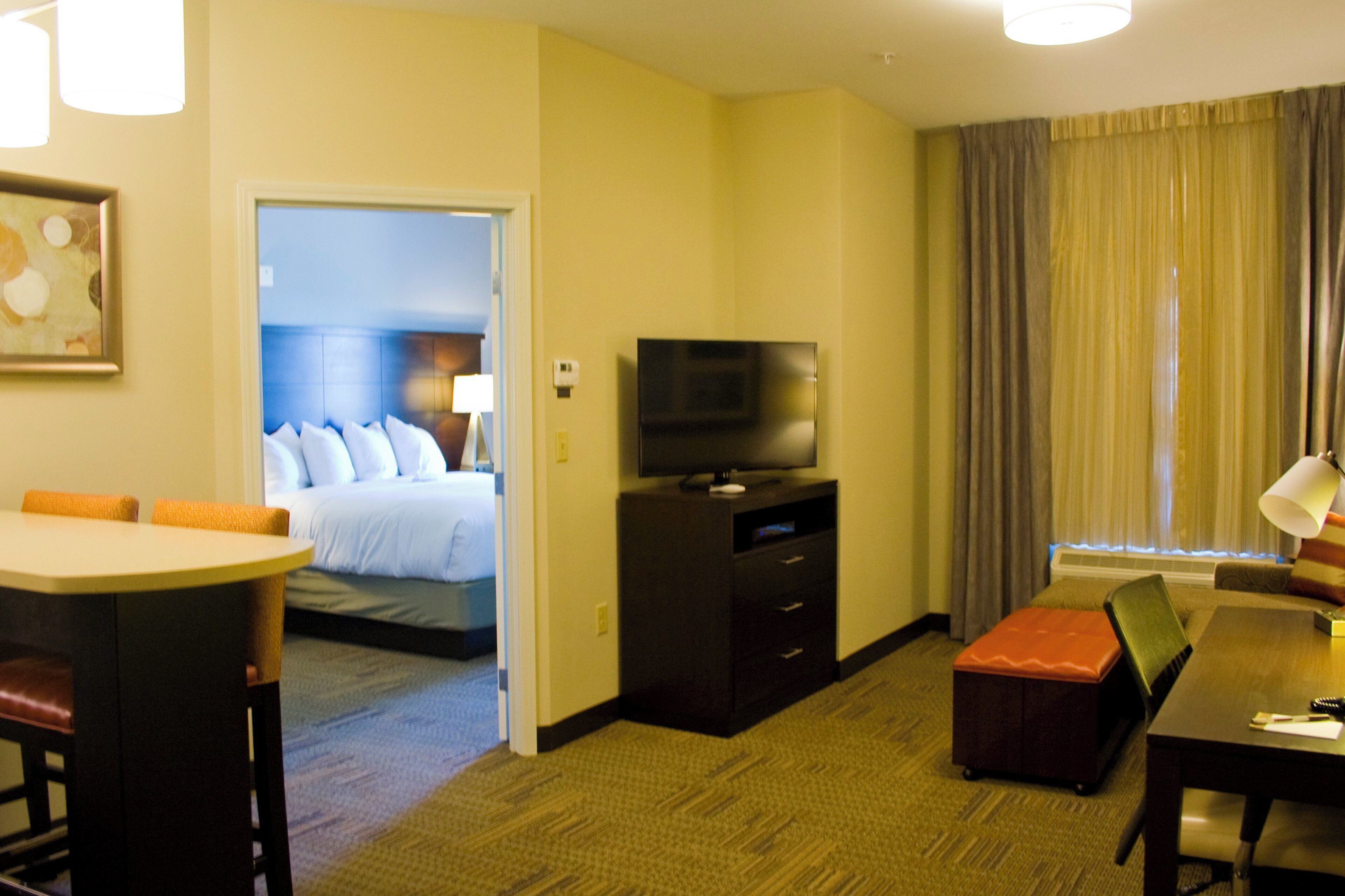 Una habitación de hotel con cama, escritorio, televisor y área de comedor.