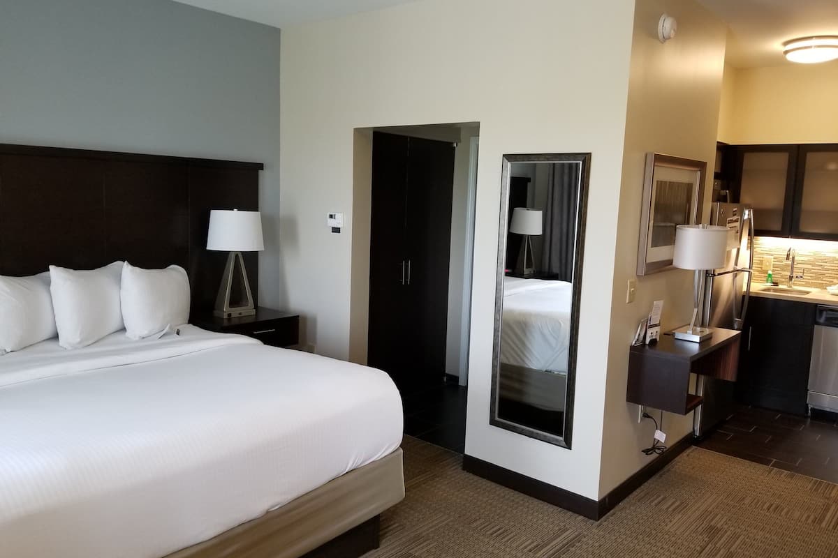 Een hotelkamer met een groot bed, nachtkastjes, een spiegel, een klein bureau met een lamp en een kitchenette.