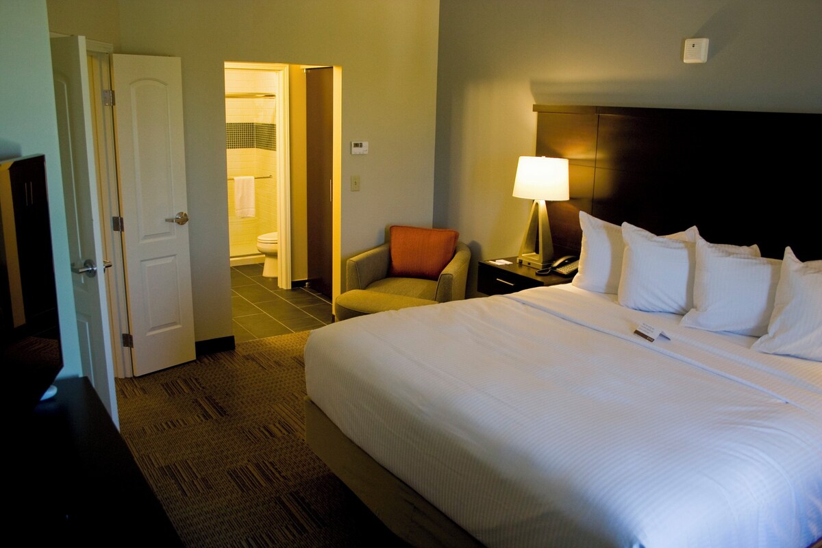 A hotel room with a bed, a chair, a nightstand, and a lamp.