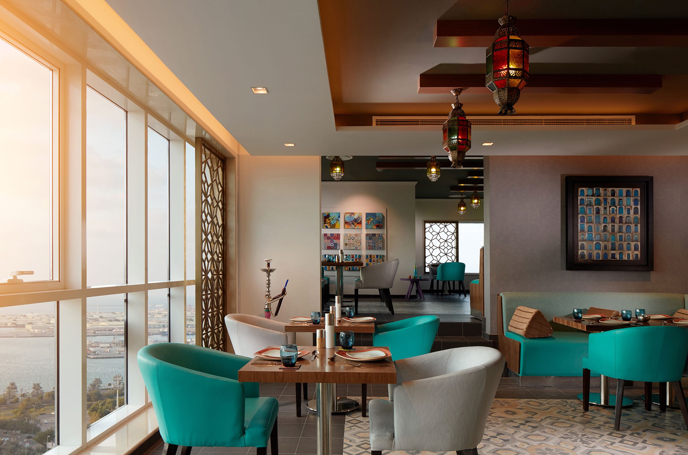 A modern dining area with teal chairs, wooden tables, and a city view through large windows.