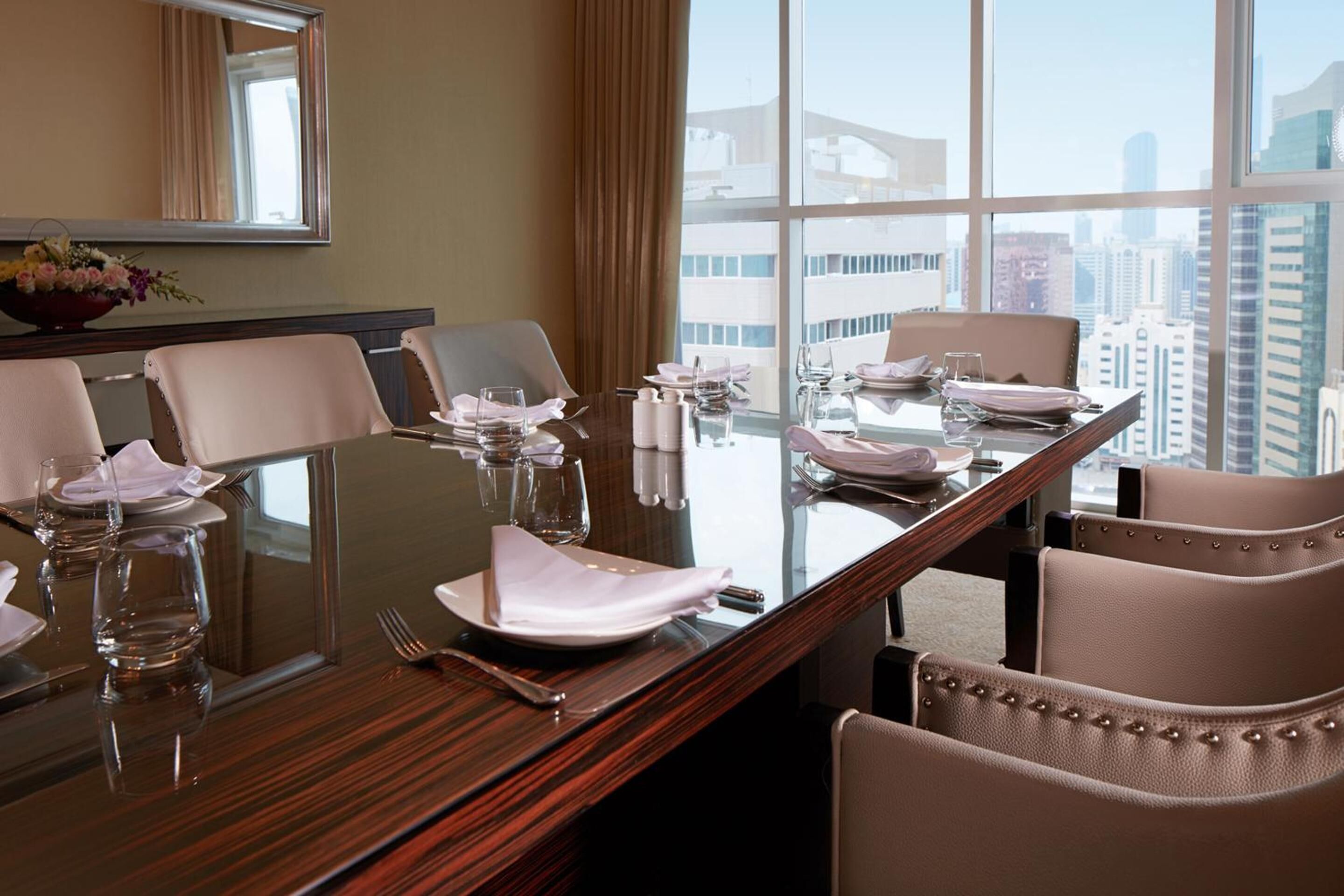 Una sala conferenze con tavolo in vetro, sedie beige e vista sulla città attraverso ampie finestre.
