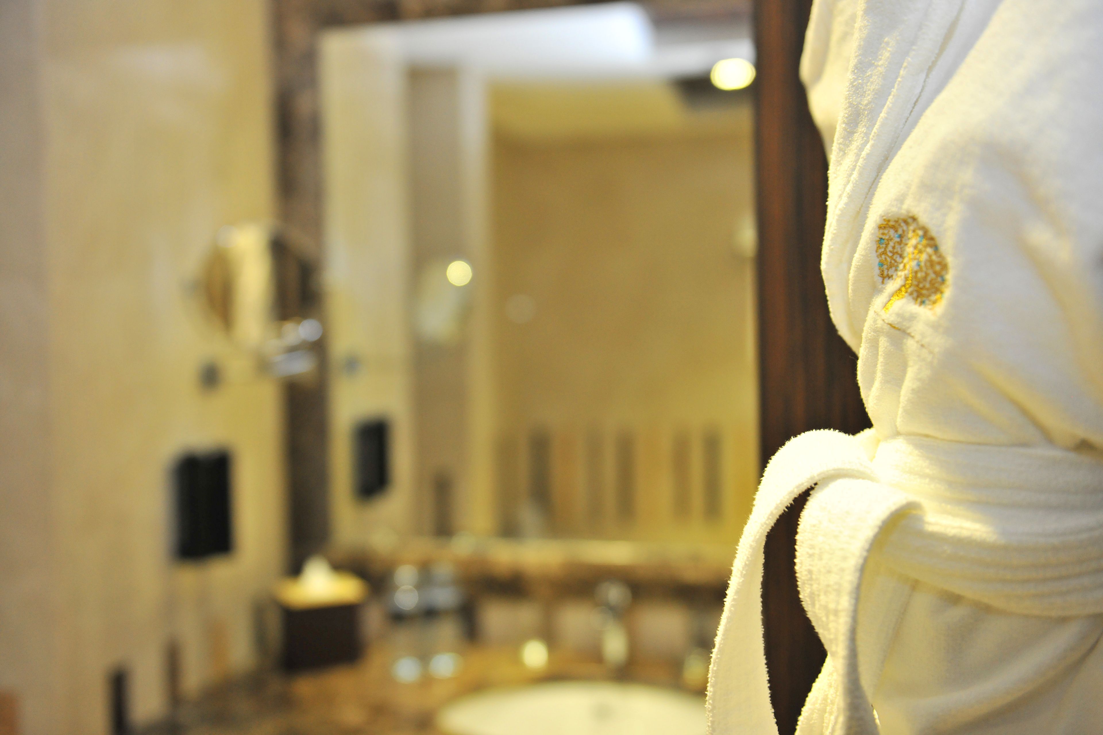 A bathroom with a sink and mirror, and a white robe with a gold emblem.