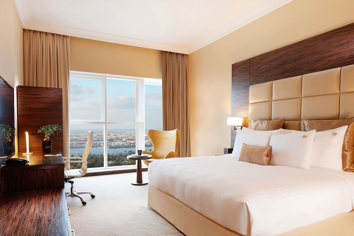 A hotel room with a large bed, a desk, a chair, a view of the city, and a window with curtains.